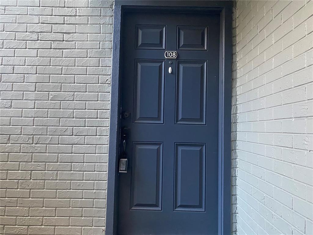 A dark blue front door with the number 108 is set between two light-colored brick walls — 3772 IDLEBROOK CIRCLE UNIT 108, CASSELBERRY, FL