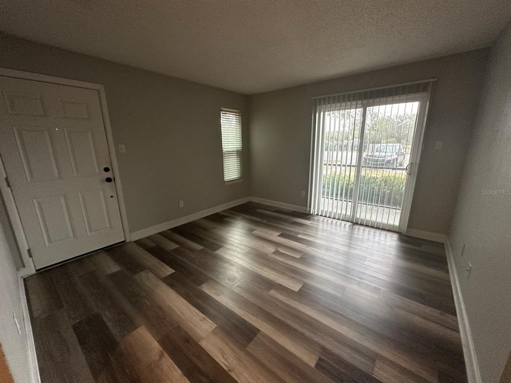 An empty room features wood-look flooring, a white entry door, a window, and sliding glass doors — 3772 IDLEBROOK CIRCLE UNIT 108, CASSELBERRY, FL