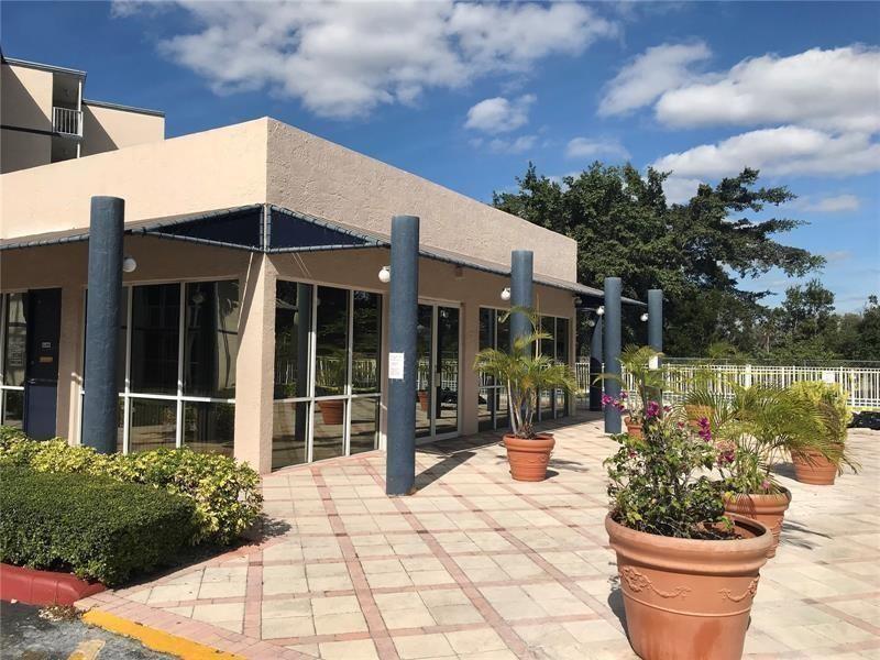 A paved patio area features potted plants, dark blue columns, and large glass windows — 7035 NW 186th Street # 111, Hialeah FL 33015, HIALEAH, FL