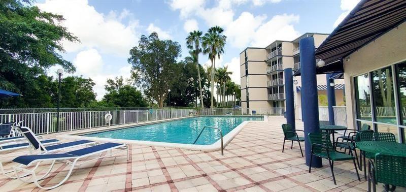 An outdoor swimming pool surrounded by lounge chairs, a patio, and a multi-story apartment building — 7035 NW 186th Street # 111, Hialeah FL 33015, HIALEAH, FL