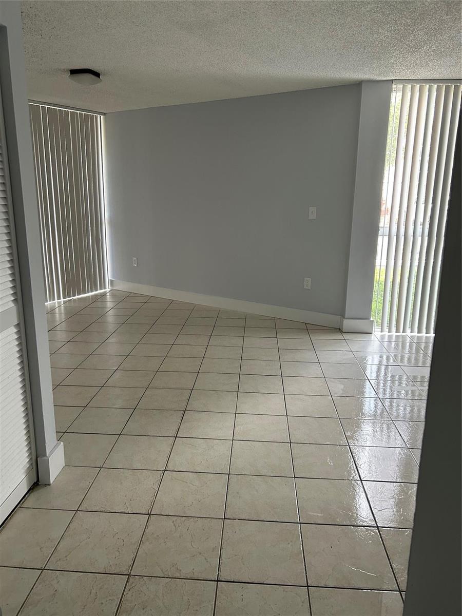 An empty room with light-colored tile flooring, gray walls, and vertical blinds on two windows — 7035 NW 186th Street # 111, Hialeah FL 33015, HIALEAH, FL
