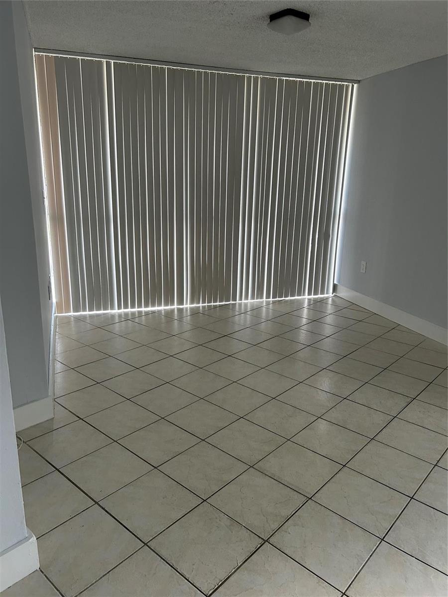 A room with light-colored tile flooring and vertical blinds covering a large sliding glass door — 7035 NW 186th Street # 111, Hialeah FL 33015, HIALEAH, FL