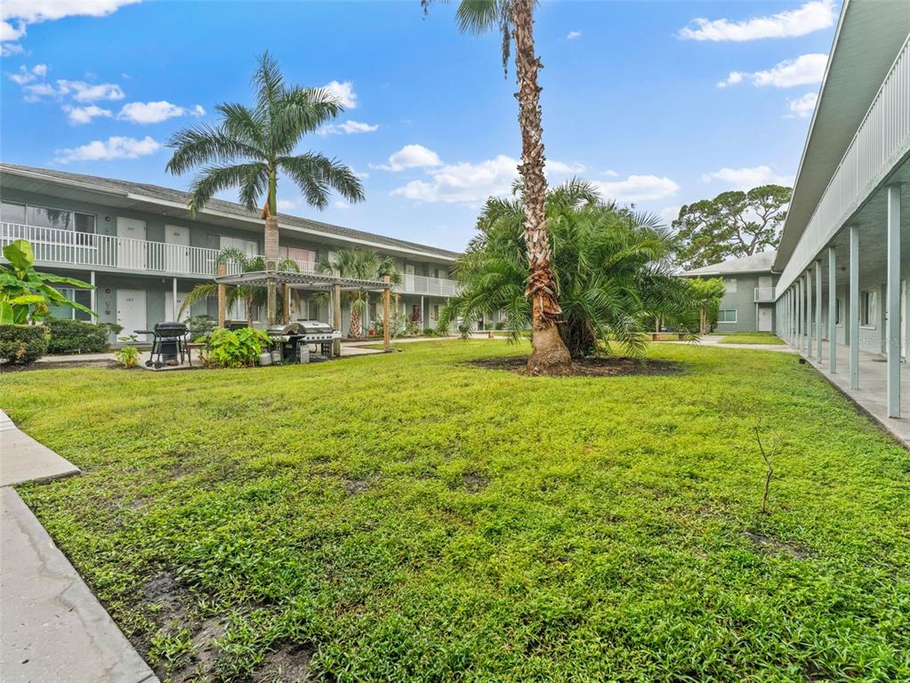 A grassy courtyard sits between two-story apartment buildings with exterior walkways and palm trees — 335 47TH AVENUE N, ST PETERSBURG, FL