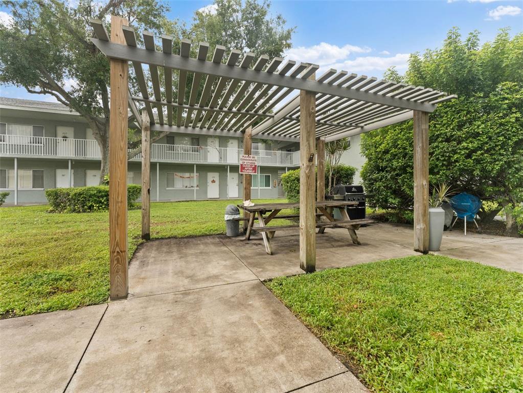 A wooden pergola covers a picnic table and grill on a concrete patio near apartments — 335 47TH AVENUE N, ST PETERSBURG, FL
