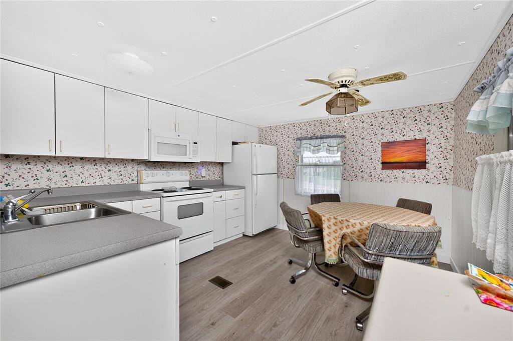 A kitchen with white cabinets, a dining table, and floral wallpaper above white wainscoting — 7514 SILAGE CIRCLE, PORT CHARLOTTE, FL