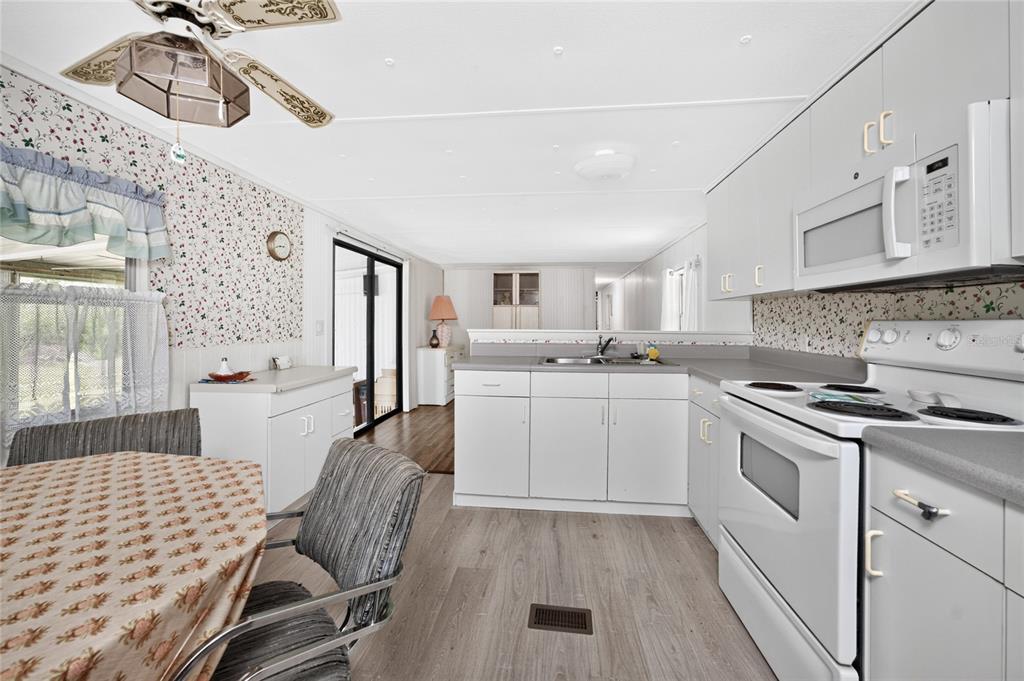 A kitchen with white cabinets, floral wallpaper, and a dining area with a ceiling fan — 7514 SILAGE CIRCLE, PORT CHARLOTTE, FL