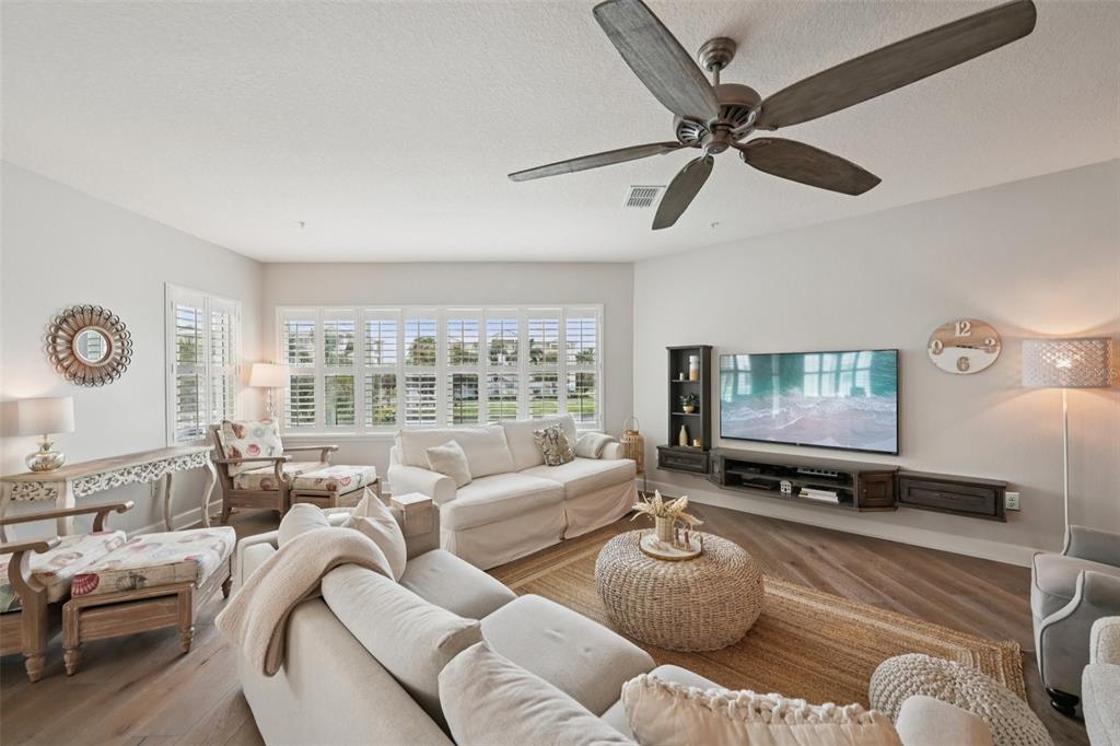 A living room features white sofas, a wooden ceiling fan, and a wall-mounted television — 3420 77TH STREET W UNIT 101, BRADENTON, FL