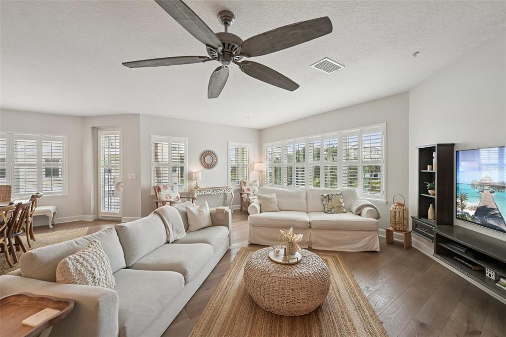 A bright living room features a white sofa, a woven ottoman, and a ceiling fan — 3420 77TH STREET W UNIT 101, BRADENTON, FL