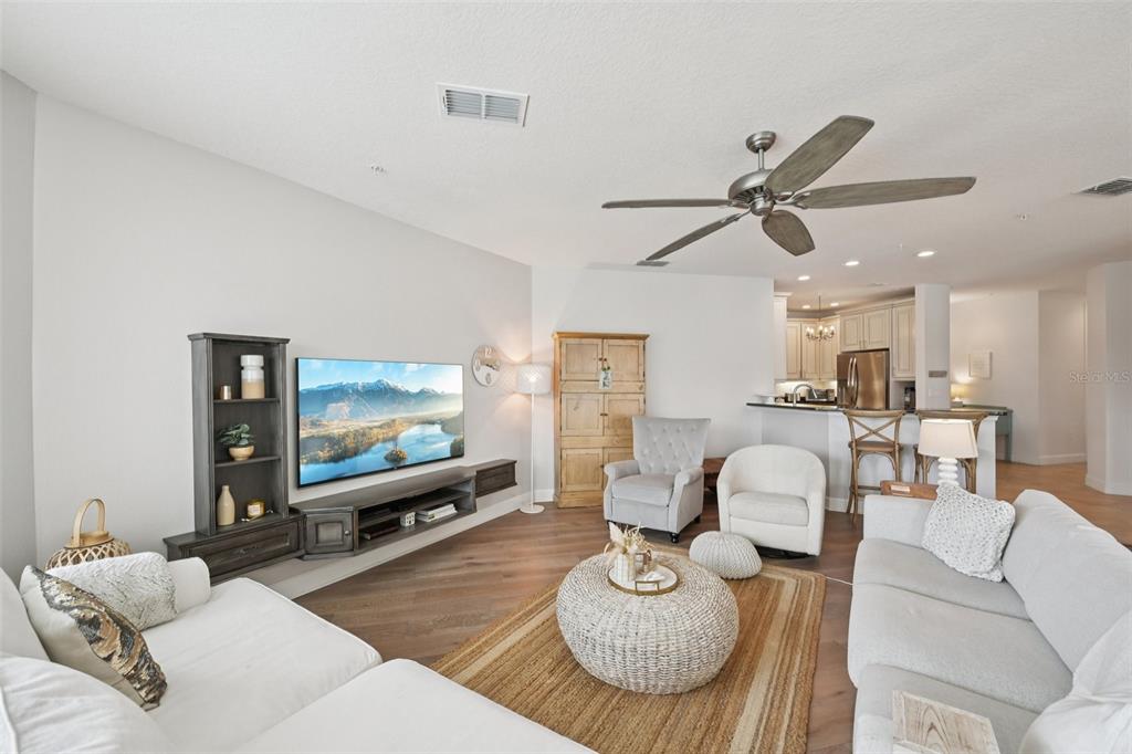 A living room features a wall-mounted television, neutral furniture, and an open kitchen area — 3420 77TH STREET W UNIT 101, BRADENTON, FL