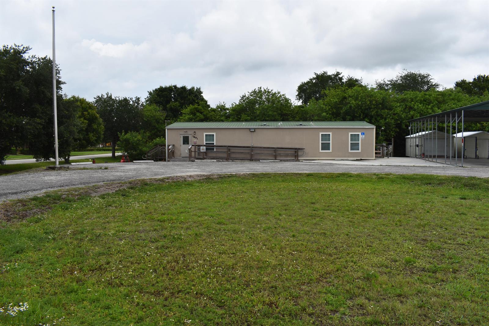 A single-story modular building with a ramp sits on a gravel lot near trees — 1893 90th Avenue, Vero Beach FL 32966, VERO BEACH, FL
