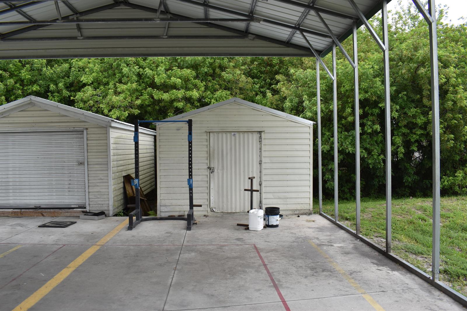 A covered outdoor concrete patio features a squat rack and two small storage sheds — 1893 90th Avenue, Vero Beach FL 32966, VERO BEACH, FL