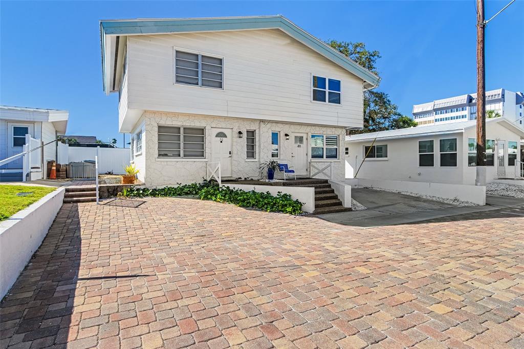 A two-story building with white siding and stone accents sits behind a brick paver driveway — 6020 MIDNIGHT PASS ROAD UNIT 49, SARASOTA, FL
