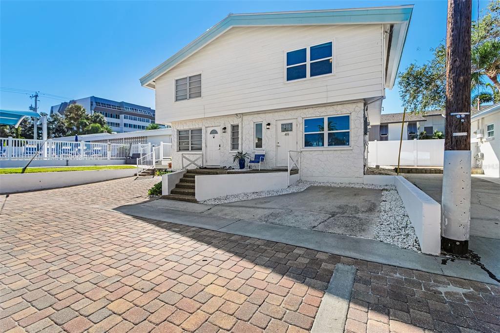 A two-story duplex with white siding and stone masonry features a brick-paved driveway — 6020 MIDNIGHT PASS ROAD UNIT 49, SARASOTA, FL