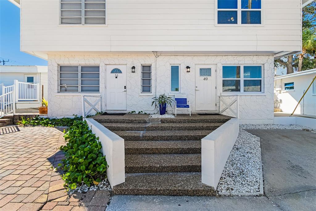 A white two-story building features two front doors numbered 49 and 50 with concrete steps — 6020 MIDNIGHT PASS ROAD UNIT 49, SARASOTA, FL