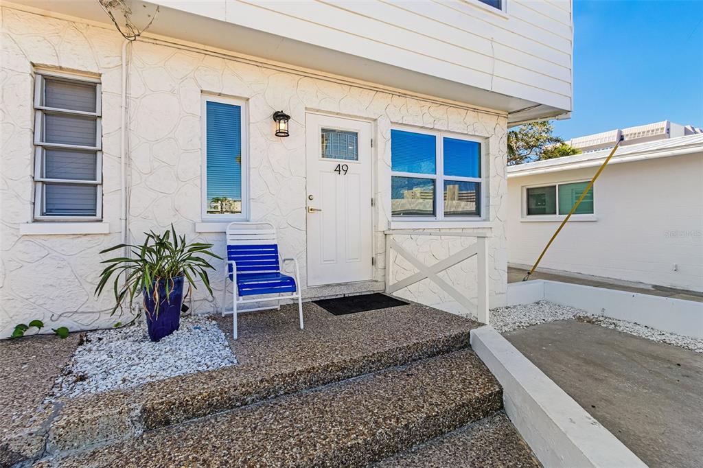 The exterior of a white building features a front door, a blue chair, and steps — 6020 MIDNIGHT PASS ROAD UNIT 49, SARASOTA, FL