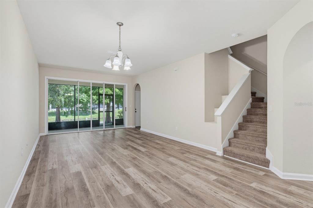 An empty living room with wood-look flooring, a chandelier, a staircase, and sliding glass doors — 4997 TOWN TERRACE S, KISSIMMEE, FL