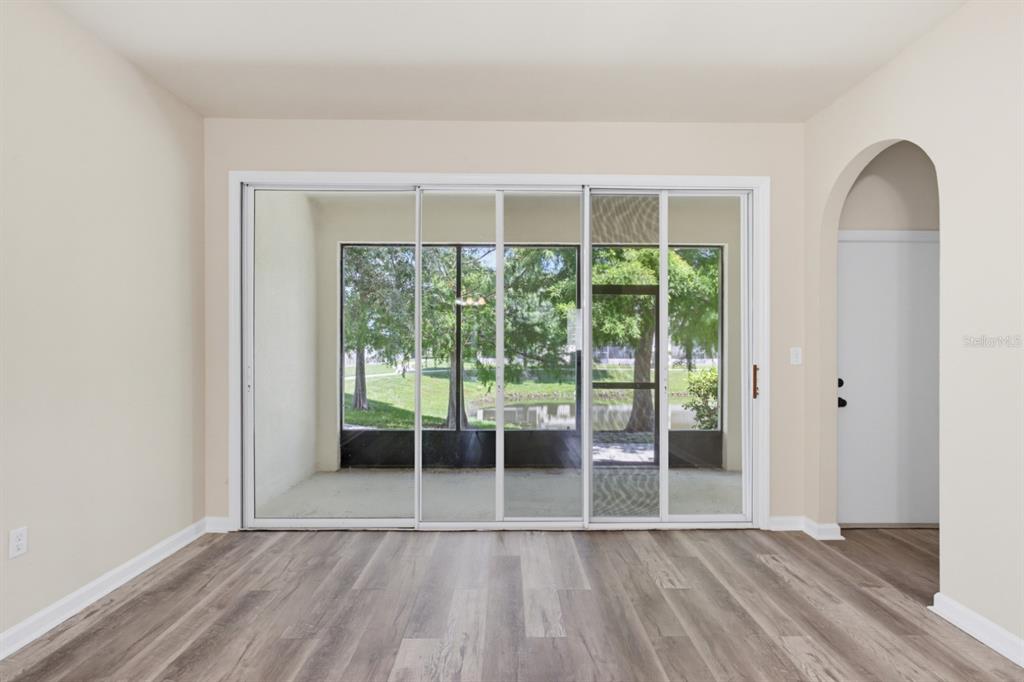 An empty room with wood-look flooring, sliding glass doors, and an arched doorway — 4997 TOWN TERRACE S, KISSIMMEE, FL