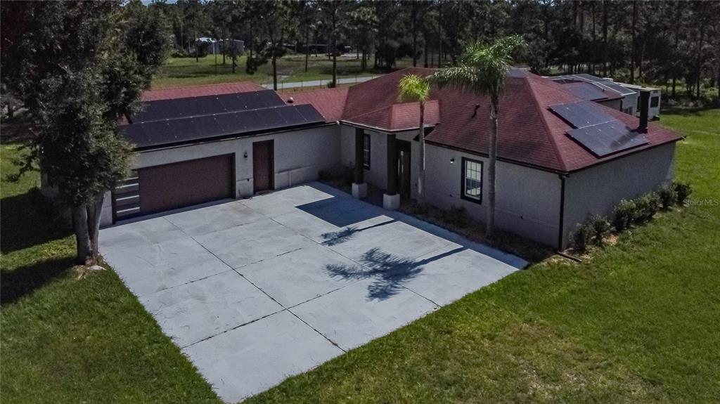 An aerial view of a single-story house with a red roof, solar panels, and driveway — 13305 LACEBARK PINE ROAD, ORLANDO, FL