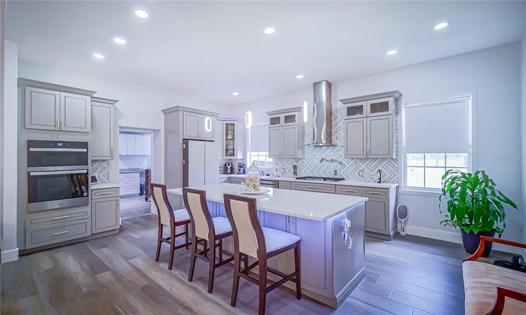 A modern kitchen features gray cabinetry, a large white island with seating, and stainless appliances — 13305 LACEBARK PINE ROAD, ORLANDO, FL