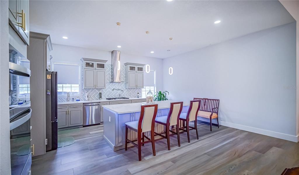 A modern kitchen features gray cabinetry, a white island with bar seating, and wood-look flooring — 13305 LACEBARK PINE ROAD, ORLANDO, FL