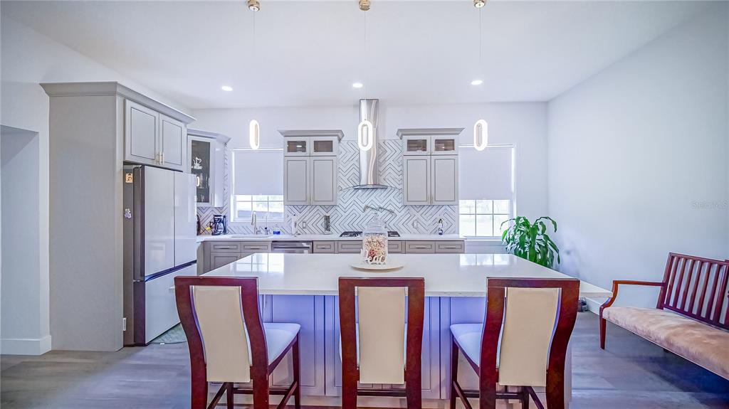 A modern kitchen features light gray cabinetry, a white island with three chairs, and herringbone backsplash — 13305 LACEBARK PINE ROAD, ORLANDO, FL