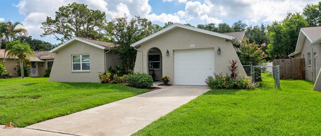 A single-story house with a beige stucco exterior, a white garage door, and a concrete driveway — 1633 ST CATHERINE DRIVE E, DUNEDIN, FL
