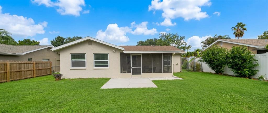 The back of a beige house features a screened-in porch and a concrete patio — 1633 ST CATHERINE DRIVE E, DUNEDIN, FL