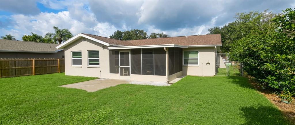 The exterior of a single-story house features a screened-in porch and a grassy backyard — 1633 ST CATHERINE DRIVE E, DUNEDIN, FL