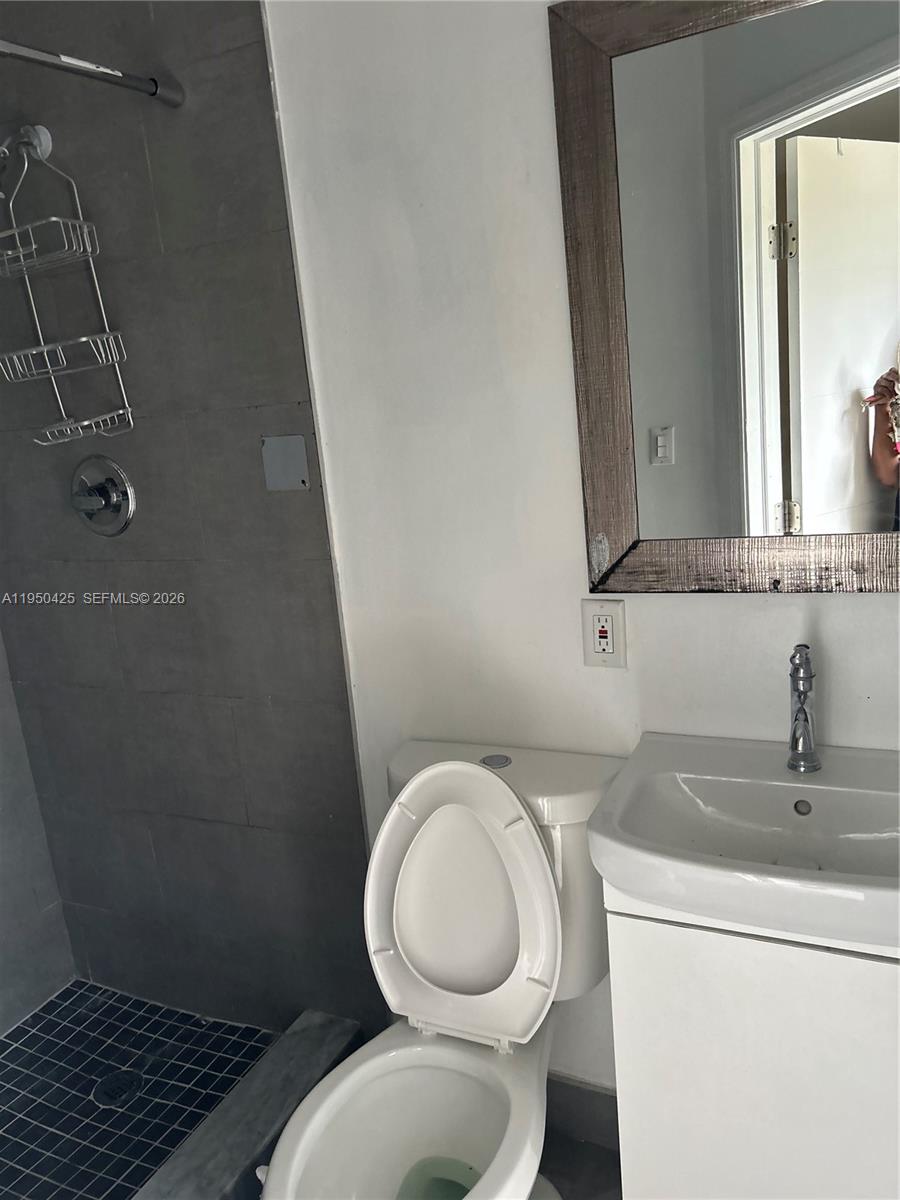 A bathroom features a tiled walk-in shower, a white toilet, and a vanity with a mirror — 2300 NW 94th St # 0, Miami FL 33147, MIAMI, FL
