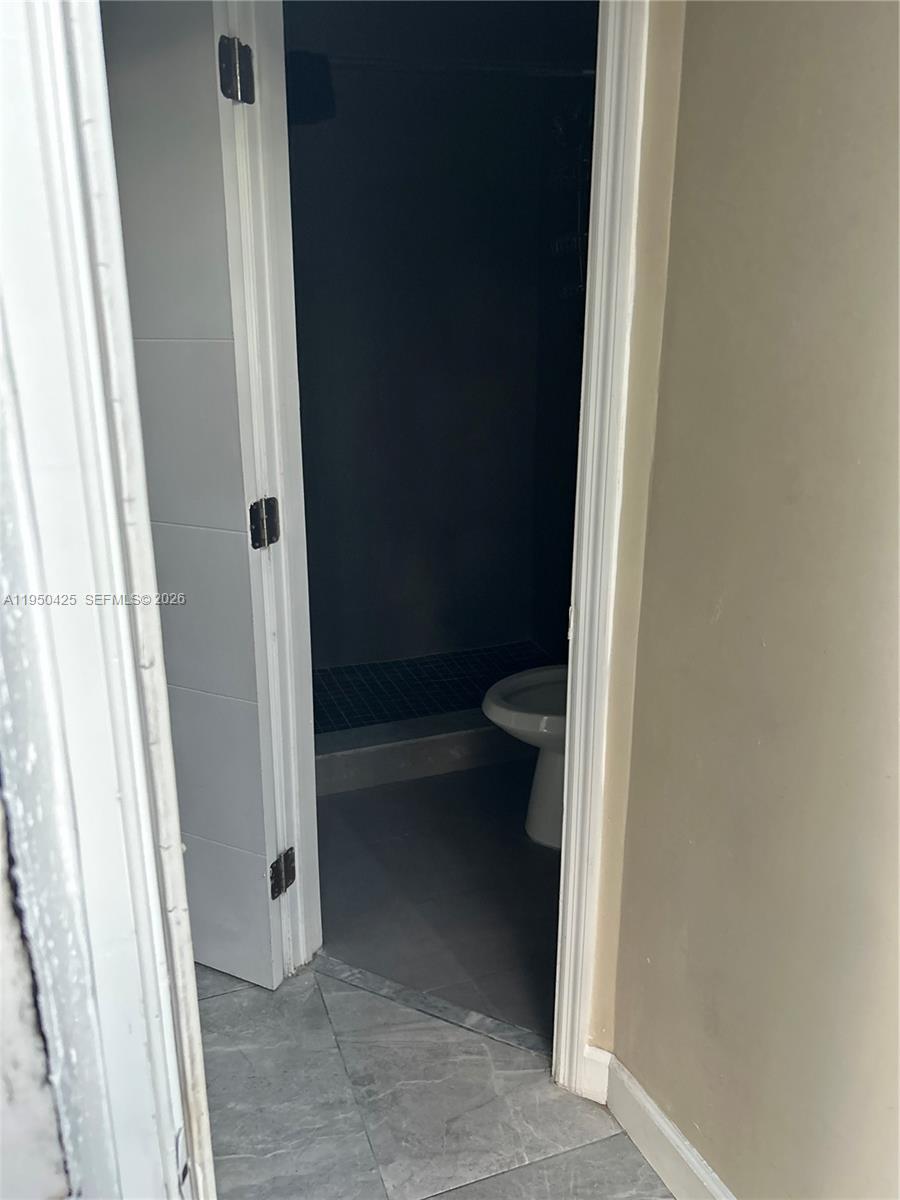A view through an open doorway shows a bathroom with gray tile flooring — 2300 NW 94th St # 0, Miami FL 33147, MIAMI, FL