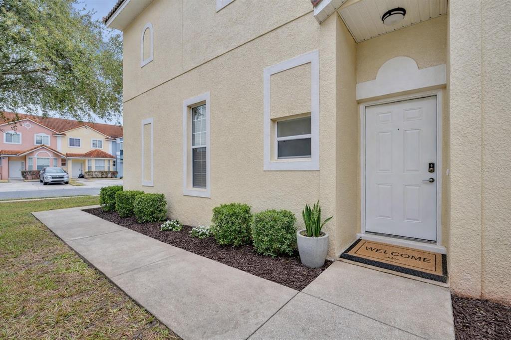A beige stucco exterior features a white front door, a welcome mat, and small shrubs — 1172 S BEACH CIRCLE, KISSIMMEE, FL