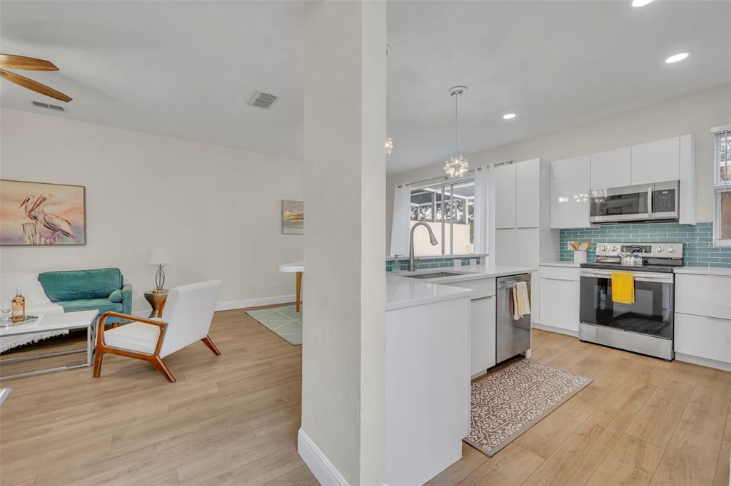 An open-concept kitchen with white cabinets and a living area with light wood flooring — 1172 S BEACH CIRCLE, KISSIMMEE, FL