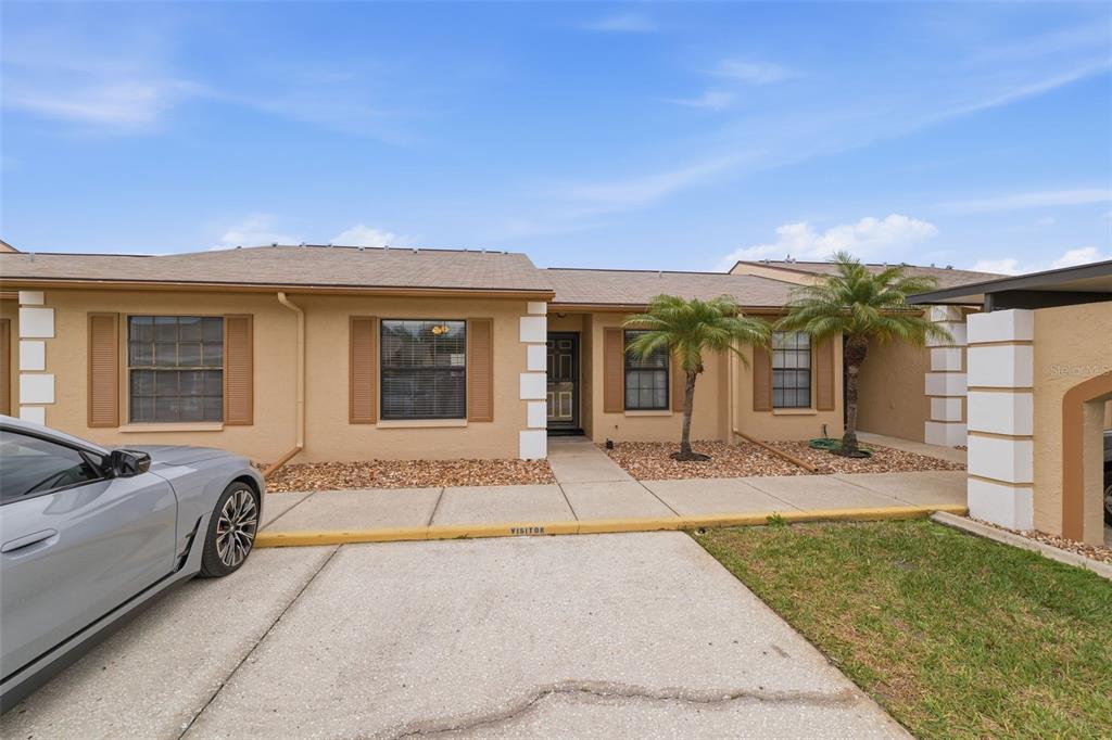 A single-story tan stucco townhouse with brown shutters, a concrete driveway, and two palm trees — 1804 RISING SUN DRIVE UNIT 1804, HOLIDAY, FL
