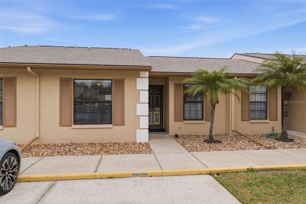 A tan, single-story townhouse exterior features brown shutters, a front walkway, and two palm trees — 1804 RISING SUN DRIVE UNIT 1804, HOLIDAY, FL
