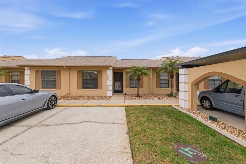 A single-story tan townhouse with a front driveway, a carport, and two palm trees — 1804 RISING SUN DRIVE UNIT 1804, HOLIDAY, FL