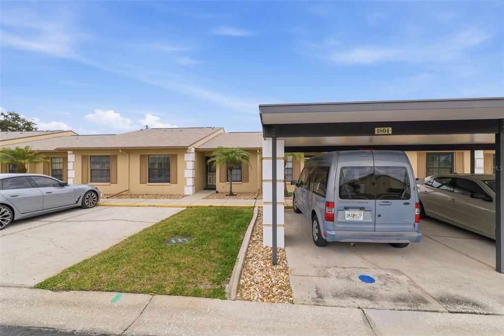 A tan single-story building features a covered carport and a small front lawn — 1804 RISING SUN DRIVE UNIT 1804, HOLIDAY, FL