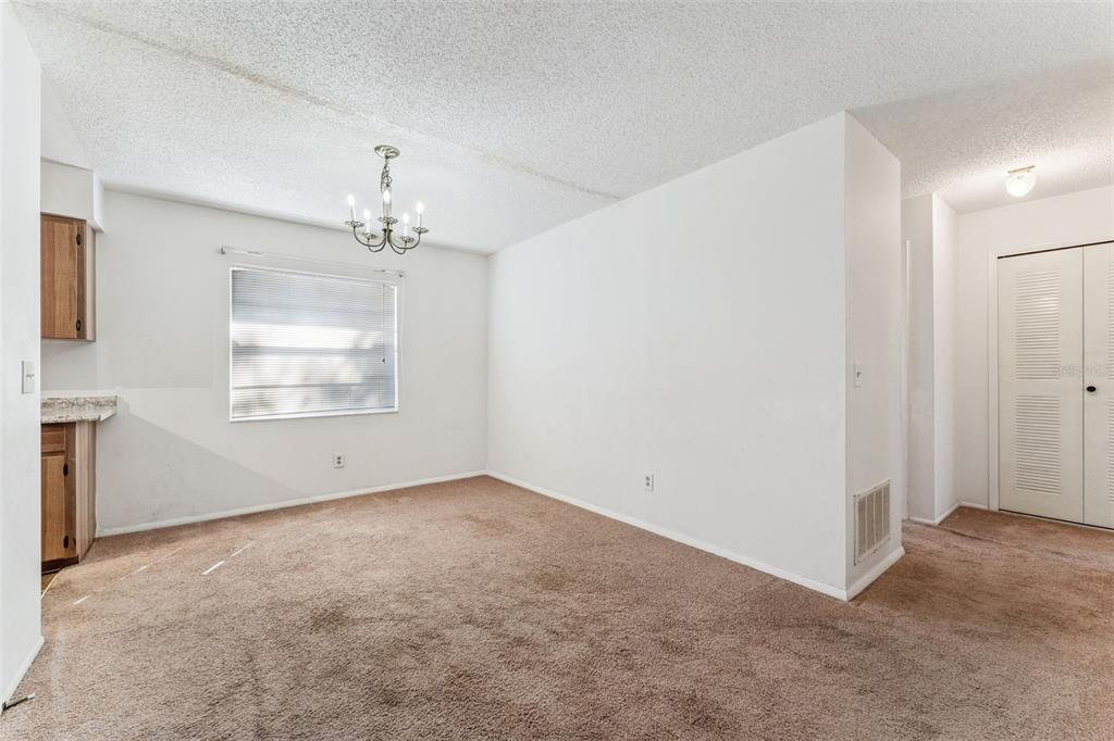 An empty dining area with brown carpet, white walls, a chandelier, and a kitchen corner — 306 LOCH LOW DRIVE, SANFORD, FL