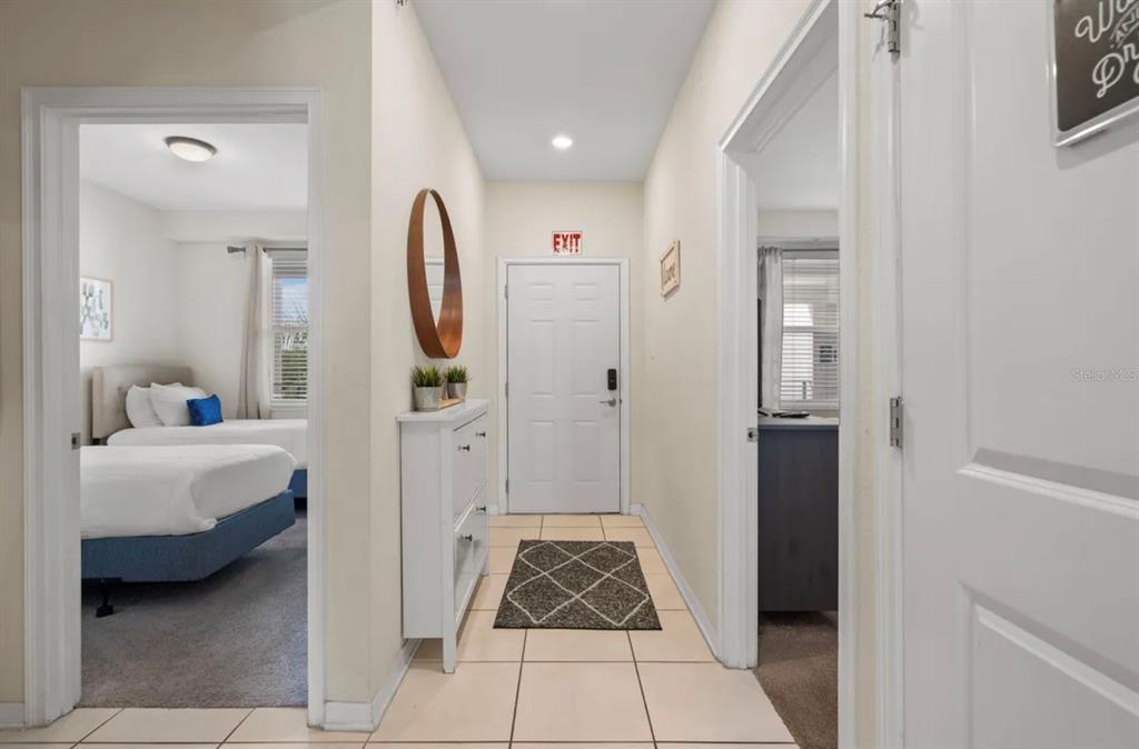 A hallway with tile flooring leads to an exit door between two bedroom doorways — 4741 CLOCK TOWER DRIVE UNIT 203, KISSIMMEE, FL