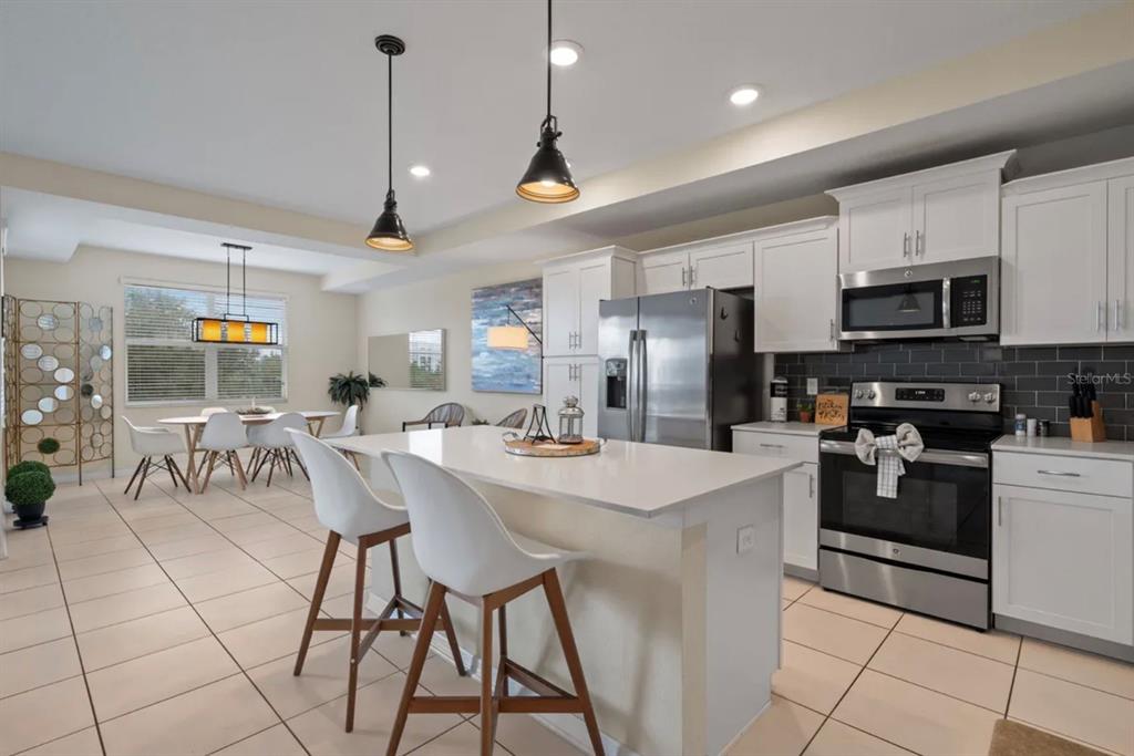 A kitchen with white cabinets, stainless steel appliances, and an island with two bar stools — 4741 CLOCK TOWER DRIVE UNIT 203, KISSIMMEE, FL