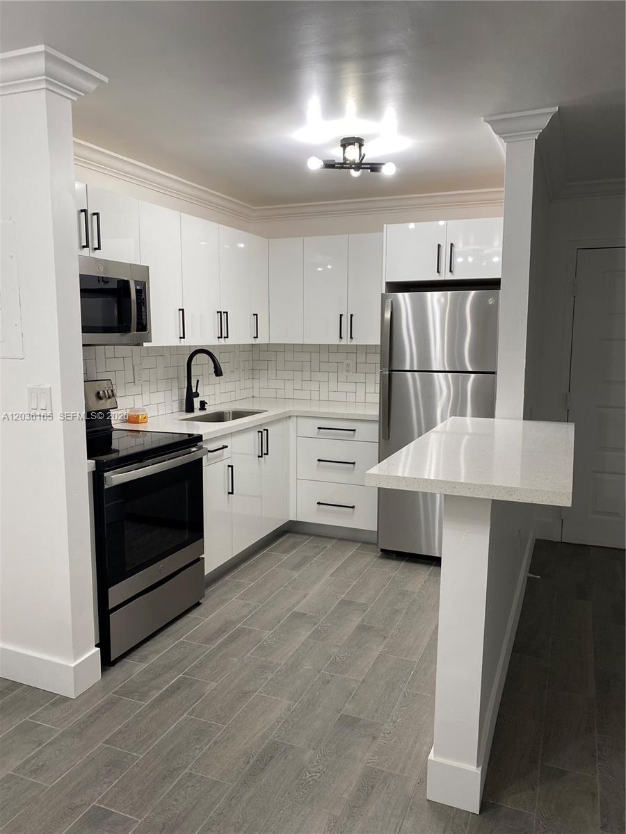 A modern kitchen features white glossy cabinets, stainless steel appliances, and a breakfast bar — 15550 SW 80th St # 207, Miami FL 33193, MIAMI, FL