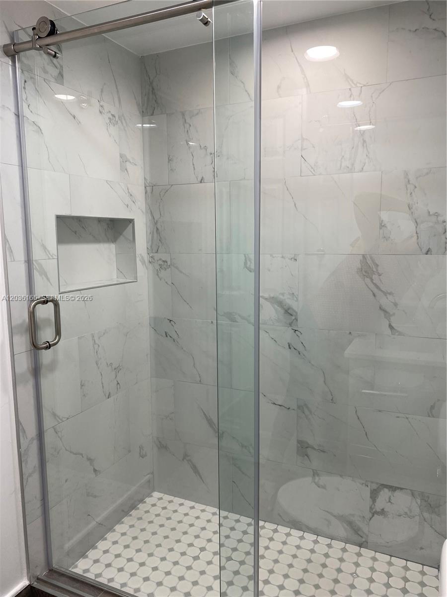 A walk-in shower features white marble-look wall tiles, a recessed niche, and hexagonal floor tiles — 15550 SW 80th St # 207, Miami FL 33193, MIAMI, FL