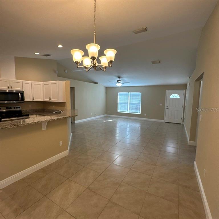An open-concept kitchen and living area with tile flooring, white cabinets, and a chandelier — 13132 SW 35TH CIRCLE, OCALA, FL