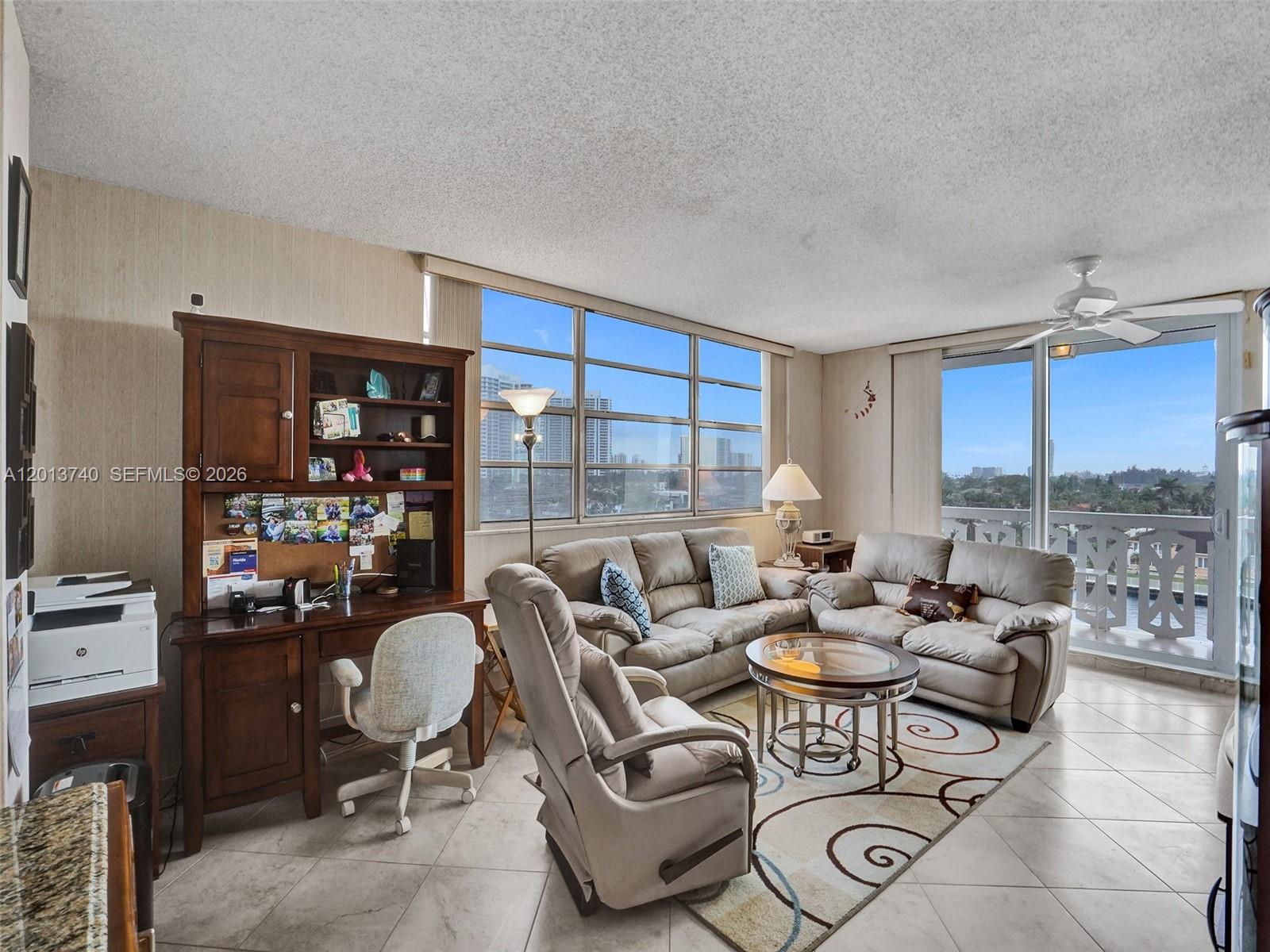 A living room features a desk, light-colored sofas, a glass coffee table, and balcony access — 3113 S Ocean Dr # 710, Hallandale Beach FL 33009, HALLANDALE BEACH, FL