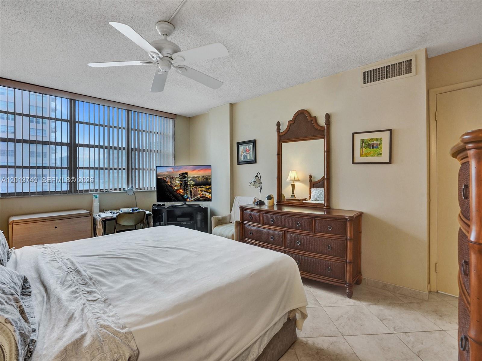 A bedroom features a bed, a wooden dresser with a mirror, and large window blinds — 3113 S Ocean Dr # 710, Hallandale Beach FL 33009, HALLANDALE BEACH, FL