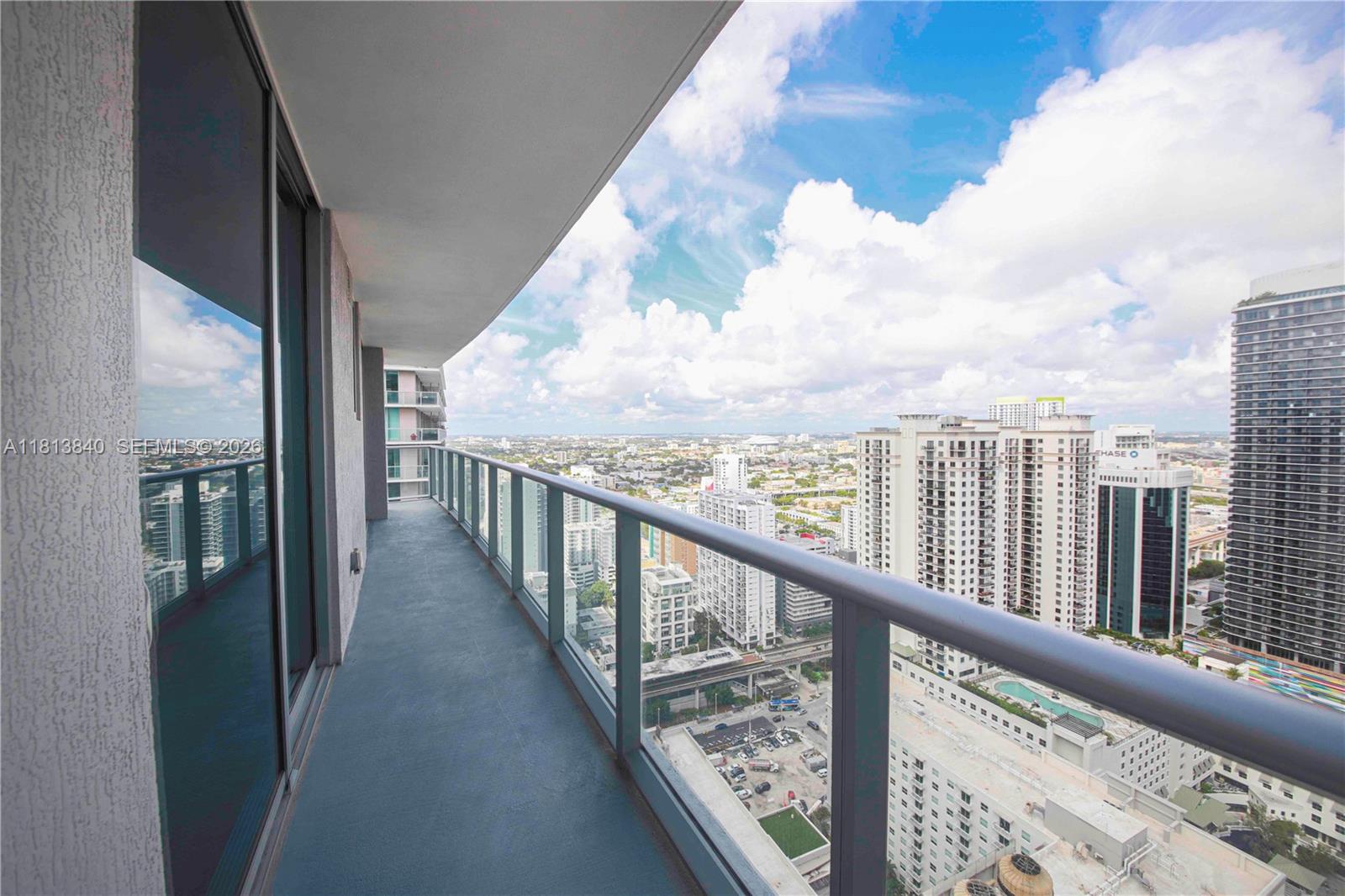 A high-rise balcony with a glass railing overlooks a dense urban cityscape under a cloudy sky — 1100 S Miami Ave # 3607, Miami FL 33130, MIAMI, FL