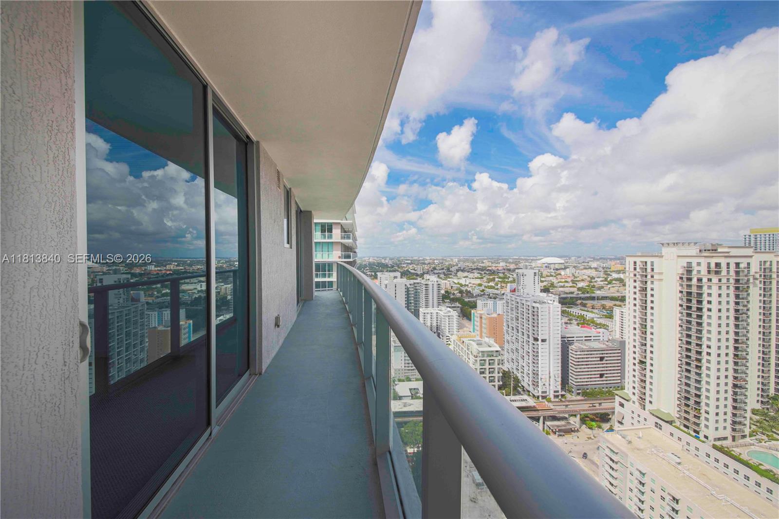 A high-rise balcony with a glass railing overlooks a dense urban cityscape under a cloudy sky — 1100 S Miami Ave # 3607, Miami FL 33130, MIAMI, FL