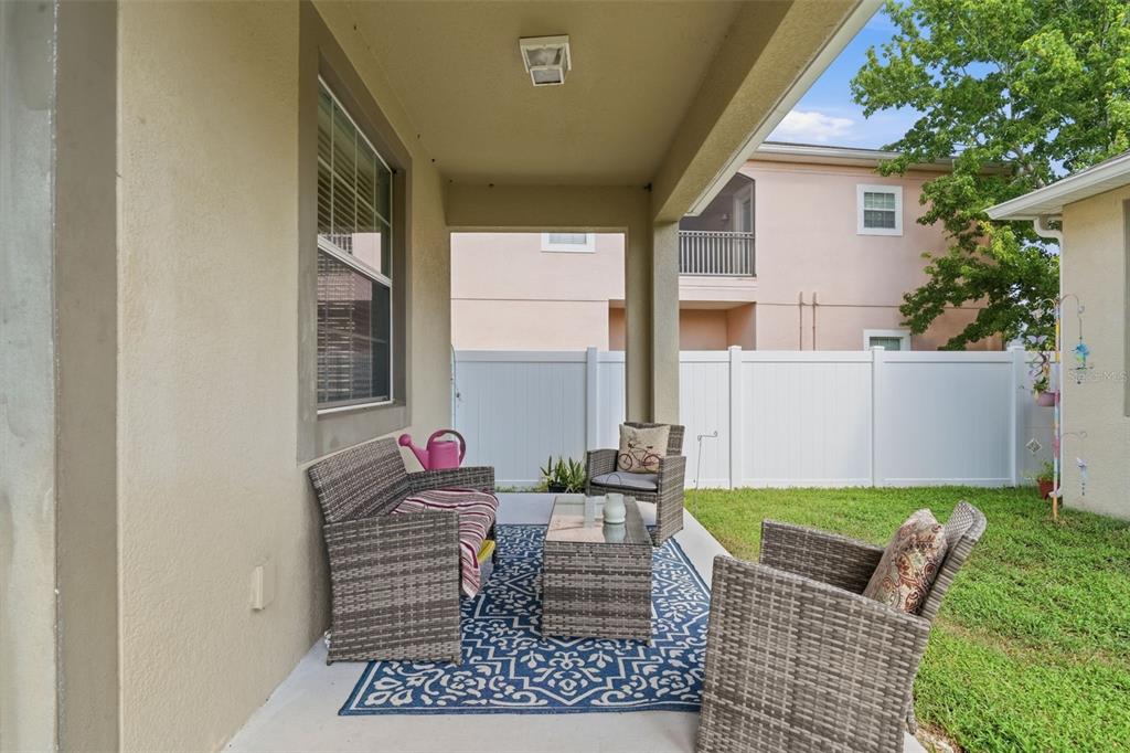 A covered patio features wicker furniture on a blue patterned rug overlooking a grassy yard — 6829 SUNDROP STREET, HARMONY, FL