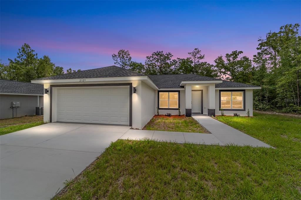 A single-story house with a white exterior, dark trim, and a two-car garage at dusk — 13737 SW 114TH PLACE, DUNNELLON, FL