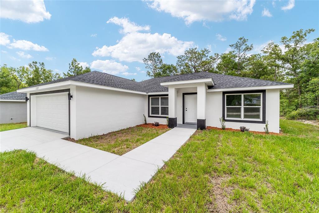 A single-story house with white stucco walls, black trim, and a concrete driveway and walkway — 13737 SW 114TH PLACE, DUNNELLON, FL