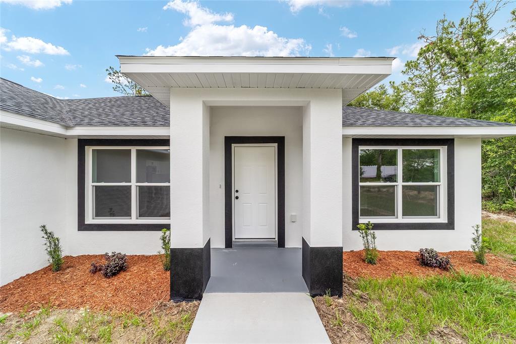 The exterior of a white house features a covered entryway and two windows with black trim — 13737 SW 114TH PLACE, DUNNELLON, FL